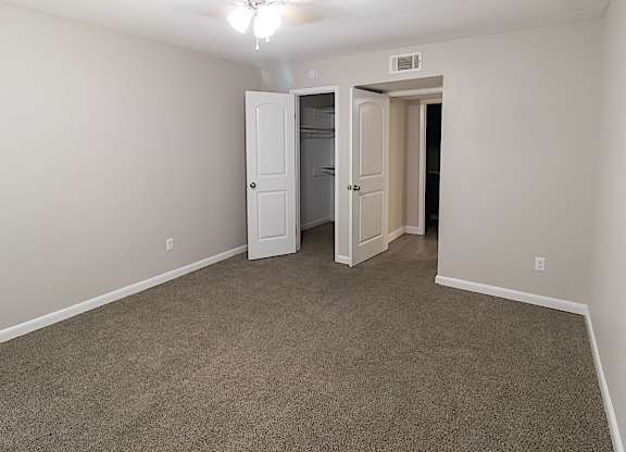 a spacious, carpeted bedroom with a walk-in closet and ceiling fan at The Forest Apartments