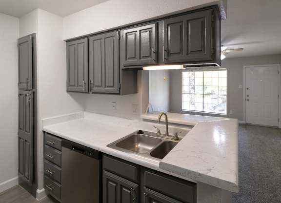 a kitchen with dark gray cabinets and white counter tops and a stainless steel sink