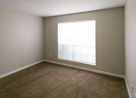 a carpeted bedroom with a large double window at The Forest Apartments