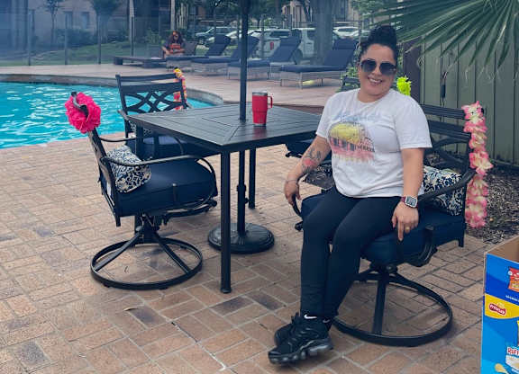 A woman sits at a table by a pool with a red cup on it.