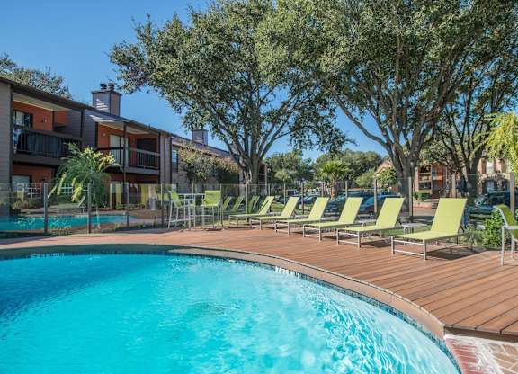 a crystal blue swimming pool surrounded by green lounge chairs and lush trees