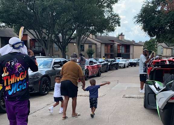 A man in a purple outfit is holding hands with a child while walking in a parking lot.