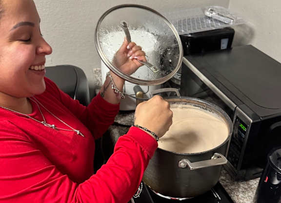 A woman in a red shirt is stirring a pot with a ladle.