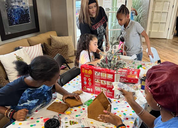 A group of people are gathered around a table with various items on it.