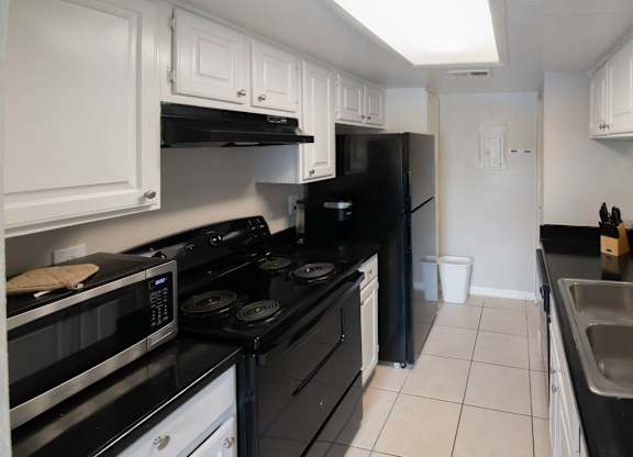 a kitchen with tiled floor, black appliances, and white cabinets