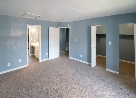 a Winford Place bedroom with blue walls, carpet, and spacious closets with built in shelving