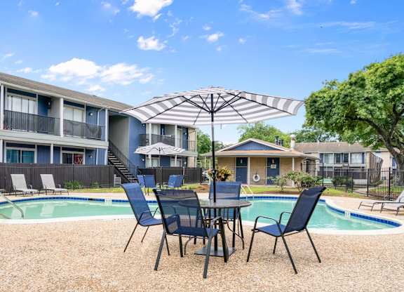 one of the two pools with a large sundeck, table, chairs, and umbrella at Pine Creek Apartments