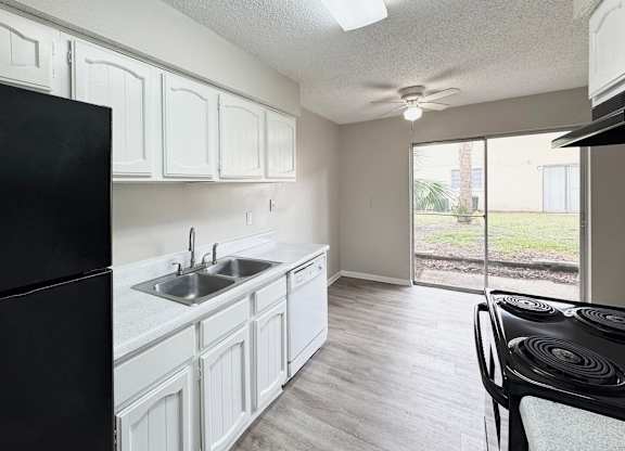 A black refrigerator stands next to a white sink in a kitchen.