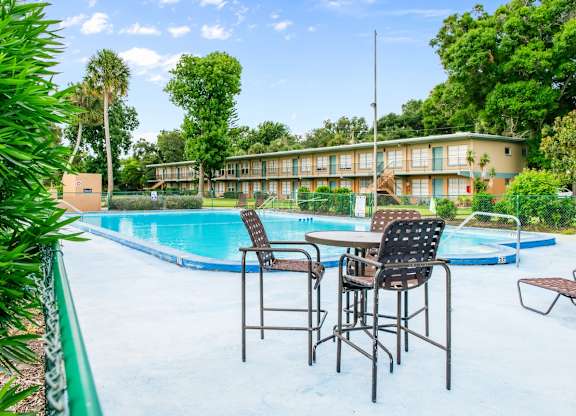 A poolside table with chairs is set up next to the Park Apartments swimming pool in Daytona Beach, FL.