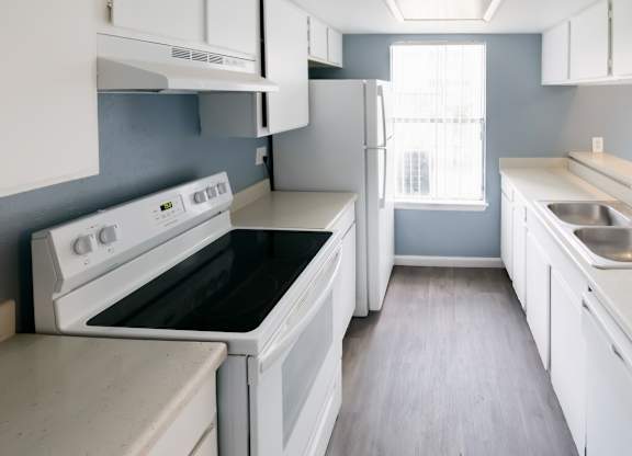 a large kitchen with efficient white appliances, white cabinets, and wood-style floors