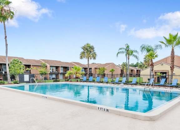 a swimming pool, sundeck, and lots of lounge chairs surrounded by tall palm trees
