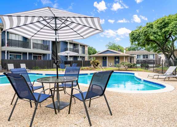 Pool side area with a table and chairs and an umbrella at Pine Creek Apartments, Houston, 77013
