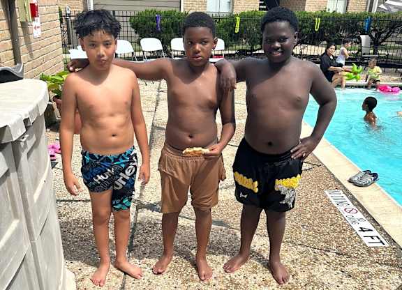 Three boys standing by a pool.