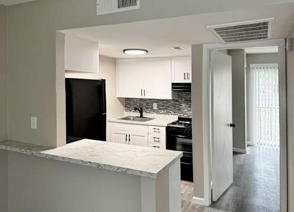 A kitchen with black appliances, white cabinets, and tile backsplash