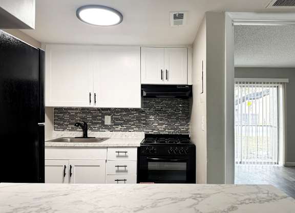 A kitchen with black appliances, tile backsplash, and white cabinets.