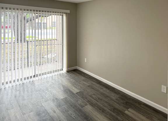 A room with a sliding glass door and wood-style flooring.
