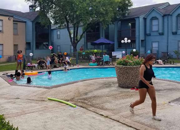 A woman is running by a pool with people swimming in it.