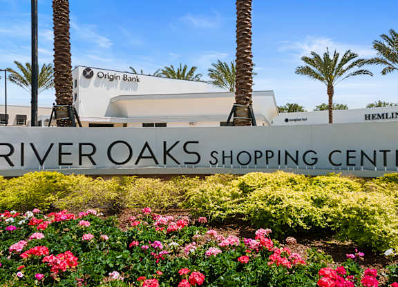 A shopping center named River Oaks Shopping Center is surrounded by palm trees and has a sign for Origin Bank.