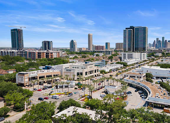 A cityscape with a mix of modern and older buildings, a clear sky, and a road with cars.