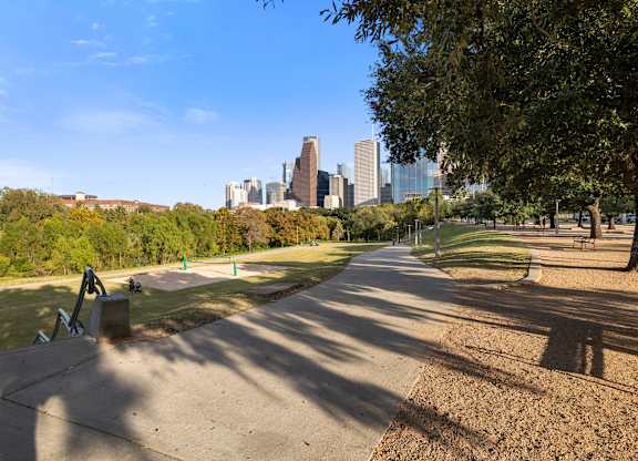 A park with a bench and a pathway leading to a city skyline.