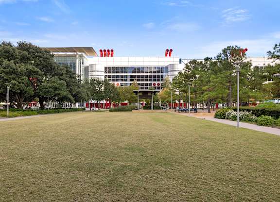 A large building with a glass facade and red accents sits behind a grassy area with trees.