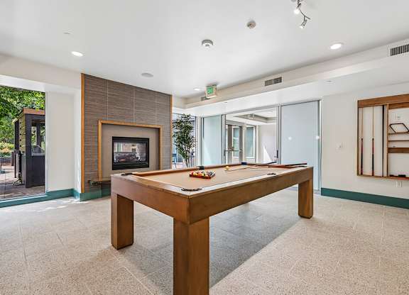 A billiard table in the middle of a room with a fireplace and sliding glass doors.
