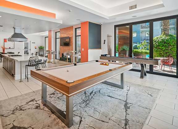 A billiard table is in the middle of a room with a kitchen area.