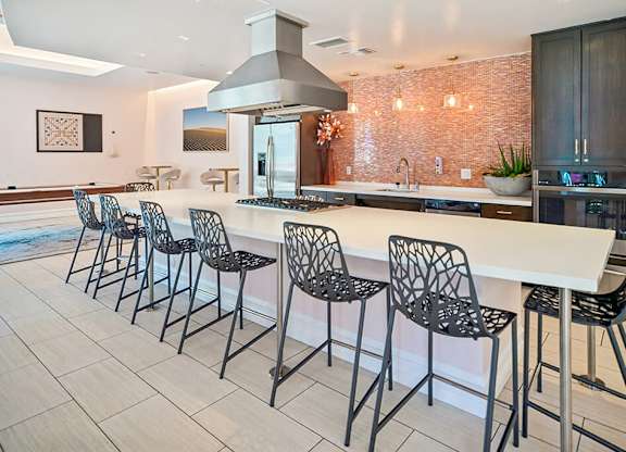 A kitchen with a long white island and black chairs.