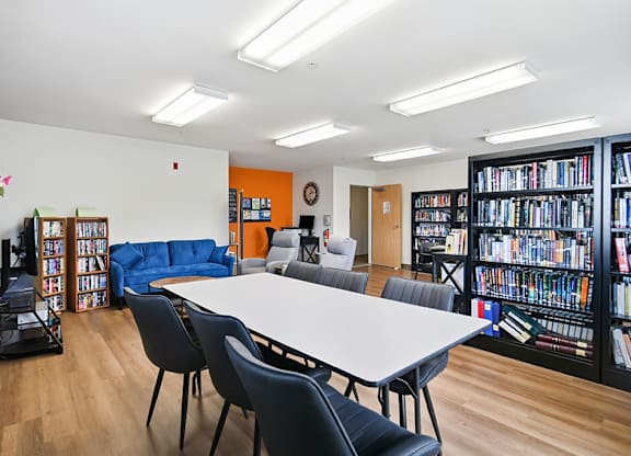 A library with a white table surrounded by chairs and bookshelves filled with books.