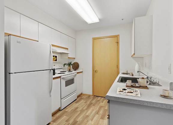 Kitchen with a white refrigerator freezer next to a stove top oven at Lakewood Meadows Apartments in Lakewood WA