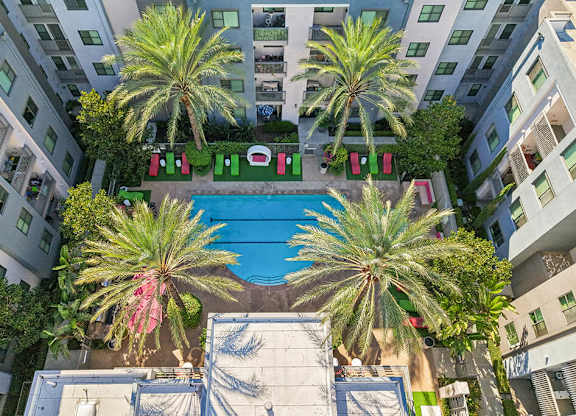 A pool surrounded by palm trees and red chairs.