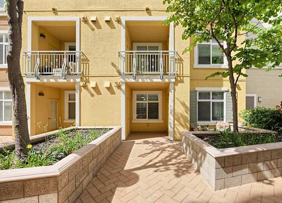 A yellow apartment building with a balcony and a small garden in front.