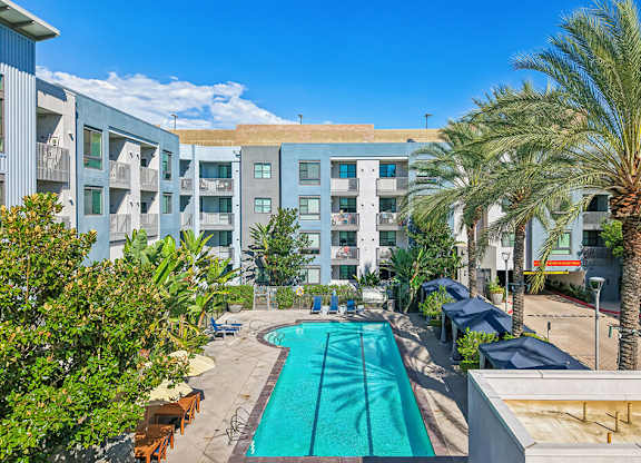 A swimming pool in front of a building surrounded by palm trees.