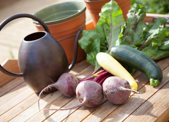 A black vase sits on a table with some vegetables.