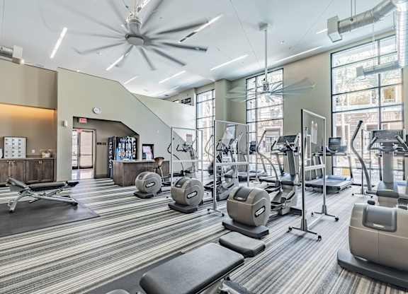 A gym with a variety of equipment including treadmills, weights, and a fan.