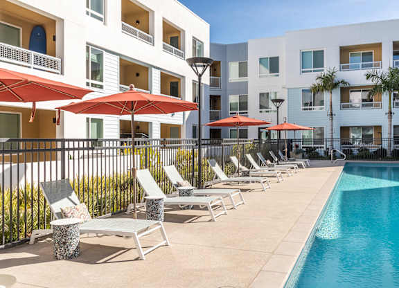 A pool area with red umbrellas and lounge chairs.