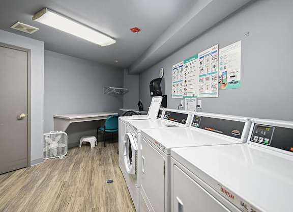 A laundry room with washers and dryers and a fan.