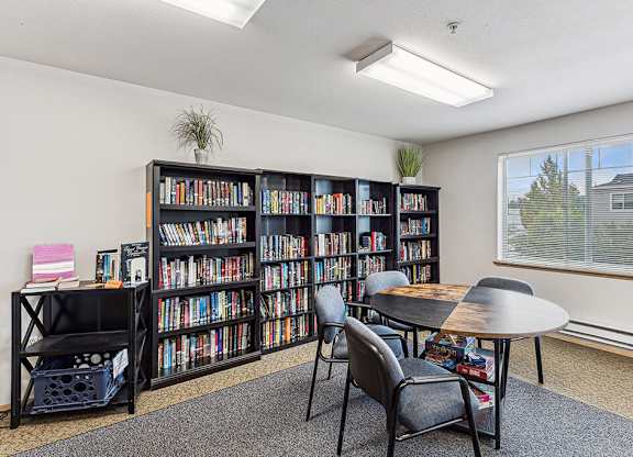 A room with a large bookshelf filled with books, a small table, and chairs.