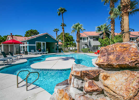 a swimming pool with a stone wall and chairs around it