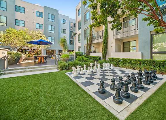 A giant chess board sits in the middle of a grassy area in front of apartment buildings.