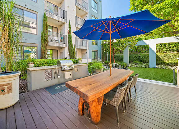 A blue umbrella is on a wooden table outside a building.