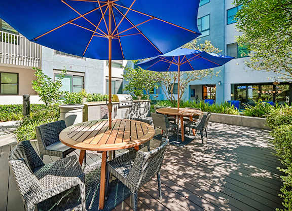 A blue umbrella shades a table and chairs on a wooden deck.