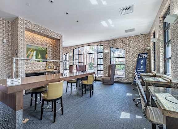 A room with a long table and chairs, a wall with a patterned wallpaper, and a large window with a view of the outside.