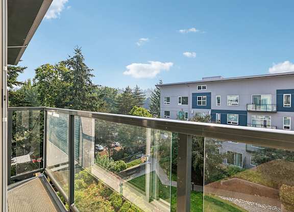 A balcony with a glass railing overlooks a building and a landscaped yard.