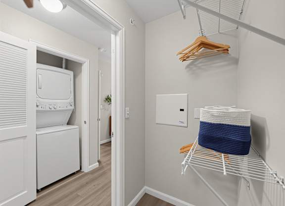 A laundry room with a washer and dryer, a basket on a rack, and a hanger with clothes.