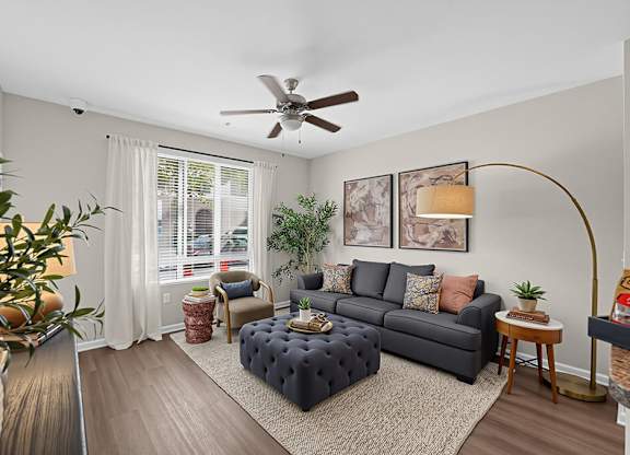 A living room with a grey couch, a coffee table, a potted plant, and a ceiling fan.