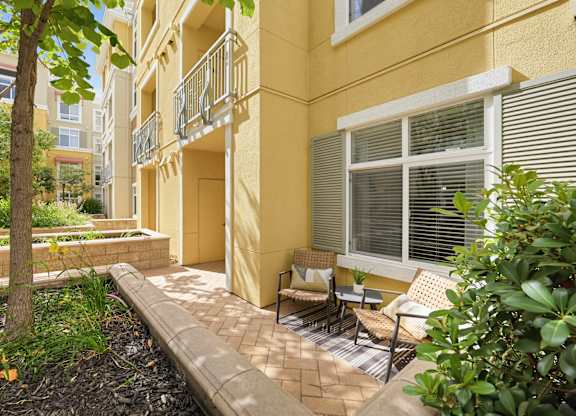 A yellow building with a balcony and a tree in front.