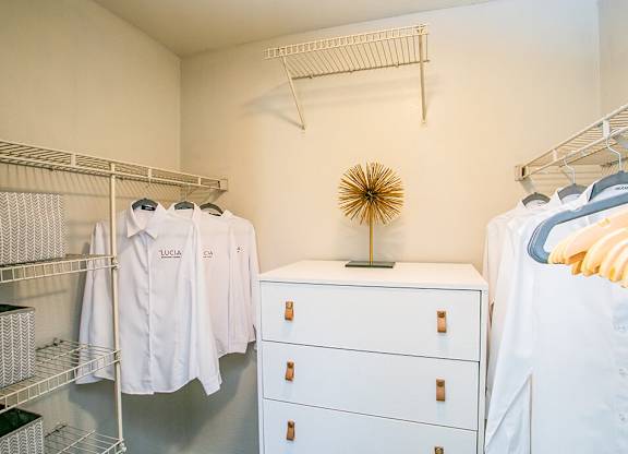 a closet with white clothes and a dresser and a rack of shirts