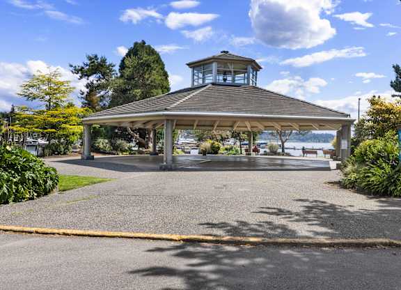 A gazebo with a tower is surrounded by greenery and a paved area.