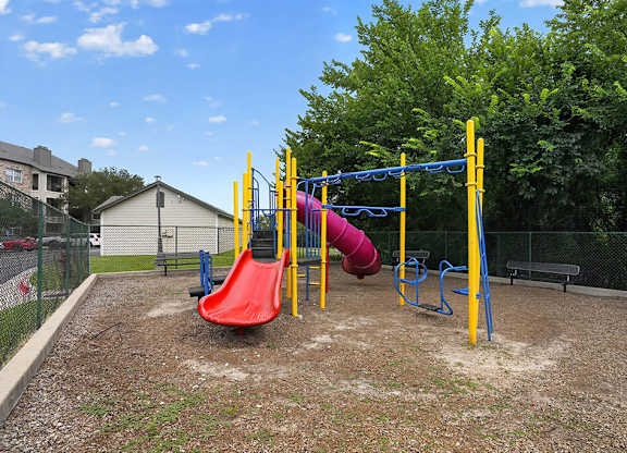 A playground with a red slide and a yellow and blue swing set.